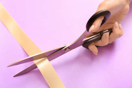 Woman cutting ribbon on color background