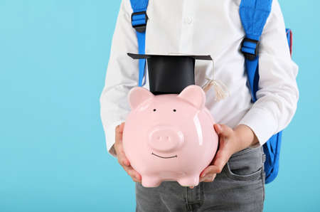 Little boy with piggy bank on color background. Concept of savings for education