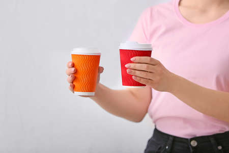 Woman with cups of hot coffee on light background, closeupの写真素材