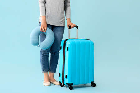 Woman with packed suitcase and travel pillow on color backgroundの写真素材