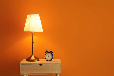 Lamp and alarm clock on table near color wallの写真素材