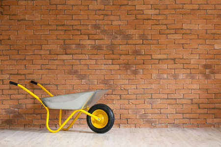 Empty wheelbarrow near brick wallの写真素材