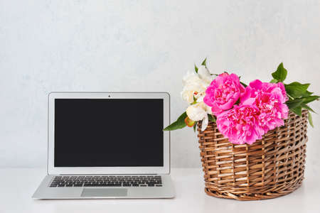 Table with laptop and peony flowers near light wallの写真素材