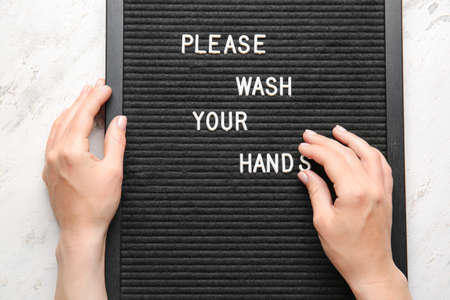 Female hands and board with text PLEASE, WASH YOUR HANDS on light backgroundの写真素材
