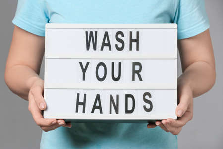 Woman holding board with text WASH YOUR HANDS on gray backgroundの写真素材