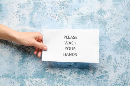 Female hand holding paper with text PLEASE, WASH YOUR HANDS on color backgroundの写真素材