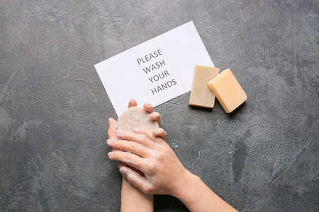 Female hands holding soap and paper with text PLEASE, WASH YOUR HANDS on gray background