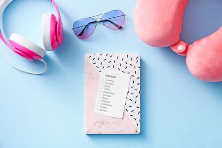 Notebook with check-list of things to pack for travel on color background