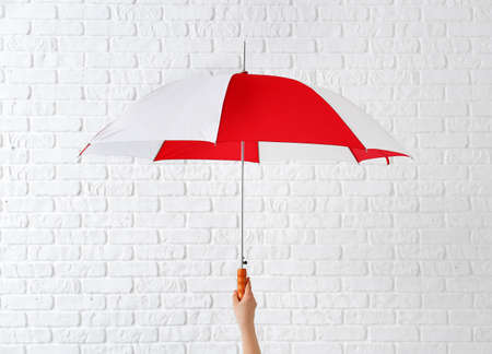 Hand with stylish umbrella on white brick background