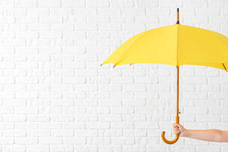 Hand with stylish umbrella on white brick backgroundの写真素材