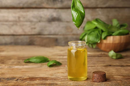 Basil essential oil dripping from leaf into bottle on tableの写真素材