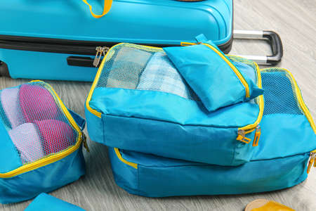 Suitcase and set of travel organizers with belongings on floor