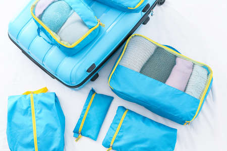 Suitcase and set of travel organizers with belongings on bed at home
