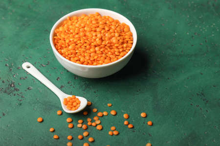 Bowl and spoon with red lentils on color background