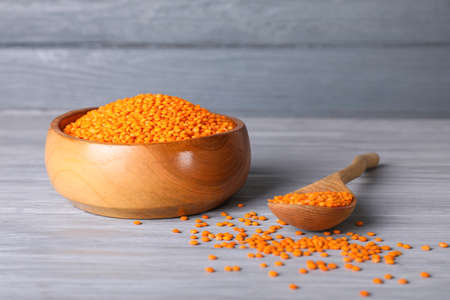 Bowl and spoon with red lentils on wooden background
