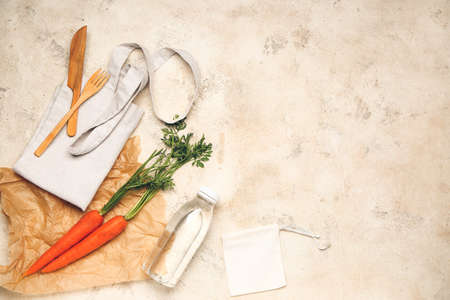 Eco bags with fresh carrots, cutlery and bottle of water on light backgroundの写真素材