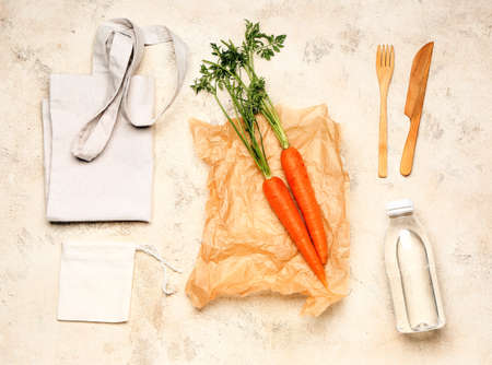 Eco bags with fresh carrots, cutlery and bottle of water on light backgroundの写真素材
