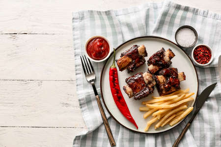 Tasty beef short ribs with chili pepper, sauce and french fries on table