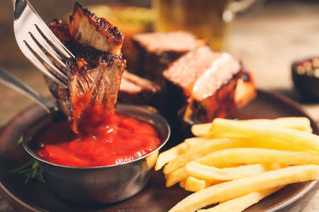 Eating of tasty beef short ribs with sauce and french fries, closeupの写真素材