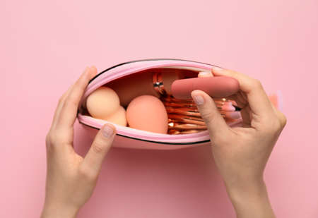 Female hands and bag with decorative cosmetics on color backgroundの写真素材