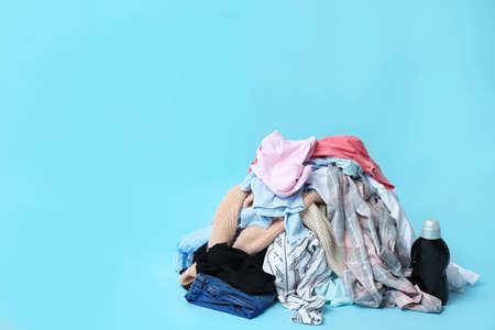 Dirty clothes and detergent on color background