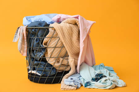 Basket with dirty clothes on color background