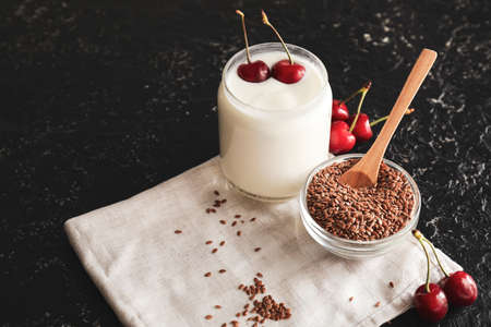 Jar of yogurt with berry and flax seeds on dark background