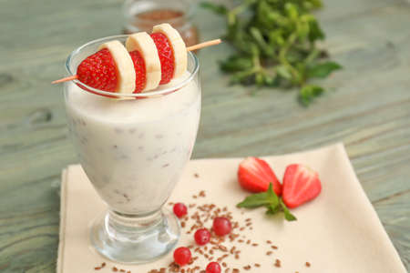Glass of yogurt with fruits and flax seeds on wooden backgroundの写真素材