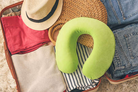 Travel pillow and open suitcase on floor in roomの写真素材