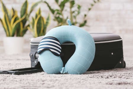 Travel pillow, sleep mask and suitcase on floor in roomの写真素材
