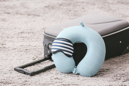 Travel pillow, sleep mask and suitcase on floor in roomの写真素材
