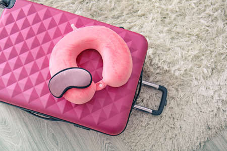Travel pillow, sleep mask and suitcase on floor in roomの写真素材