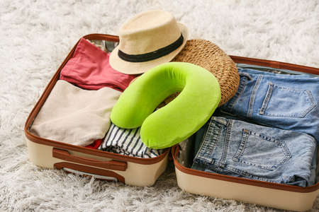 Travel pillow and open suitcase on floor in roomの写真素材