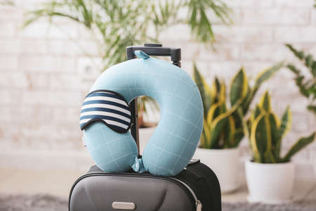 Travel pillow, sleep mask and suitcase on floor in roomの写真素材