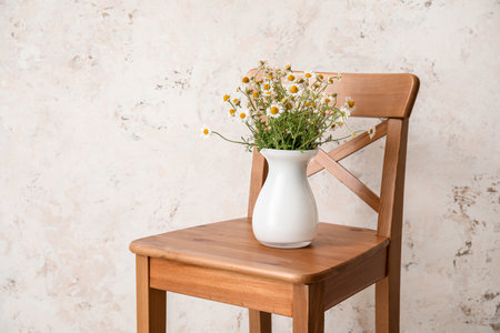 Vase with beautiful chamomiles on chair against light backgroundの写真素材