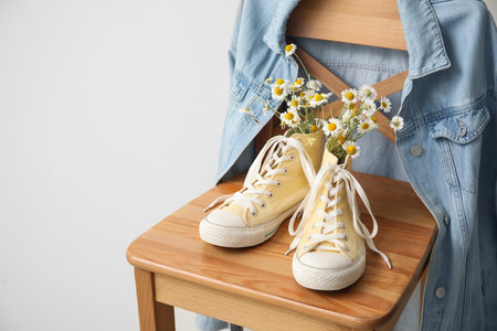 Shoes with beautiful chamomiles on chair against light backgroundの写真素材