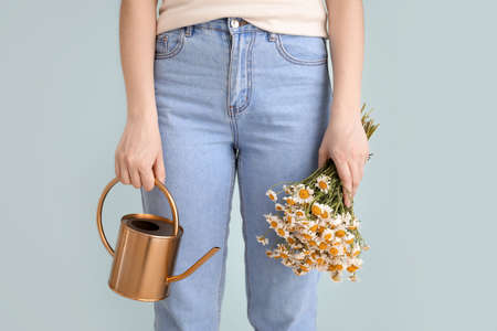 Woman with watering can and chamomiles on gray background