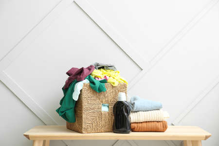 Basket with dirty clothes on table near light wall