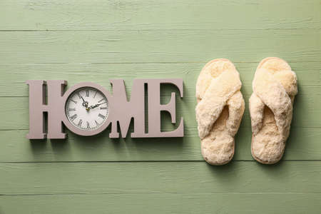 Pair of soft slippers and decorative clock on wooden backgroundの写真素材