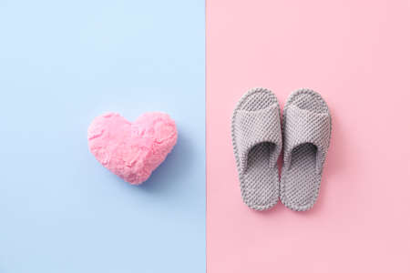 Pair of soft slippers and plush heart on color background