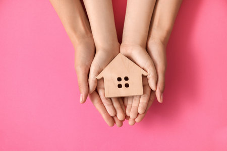 Hands of family with small house on color backgroundの写真素材