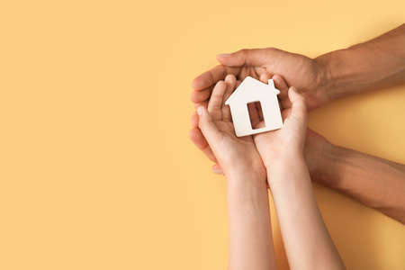 Hands of family with small house on color backgroundの写真素材