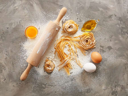 Raw pasta with ingredients and rolling pin on grunge background