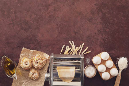 Pasta machine with ingredients on color background
