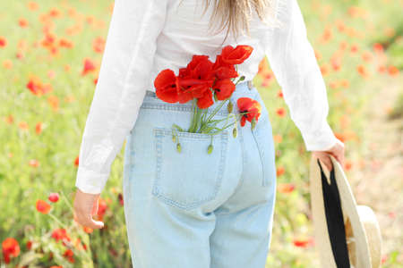 Beautiful young woman with poppy flowers in field