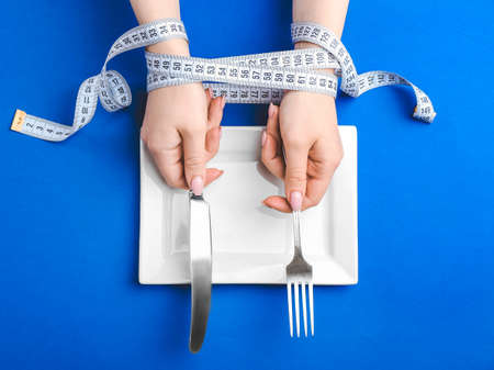 Female hands with measuring tape, empty plate and cutlery on color background. Concept of anorexiaの写真素材