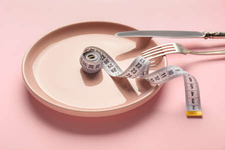 Plate with measuring tape and cutlery on color background. Concept of anorexia