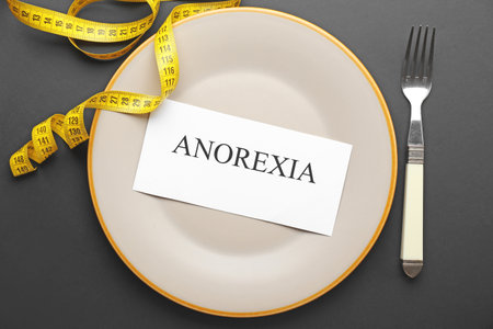 Plate with word ANOREXIA and measuring tape on dark backgroundの写真素材