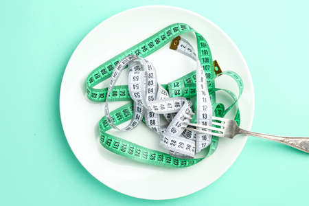 Plate with measuring tapes and fork on color background. Concept of anorexia
