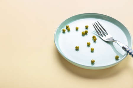 Plate with peas and fork on color background. Concept of anorexia